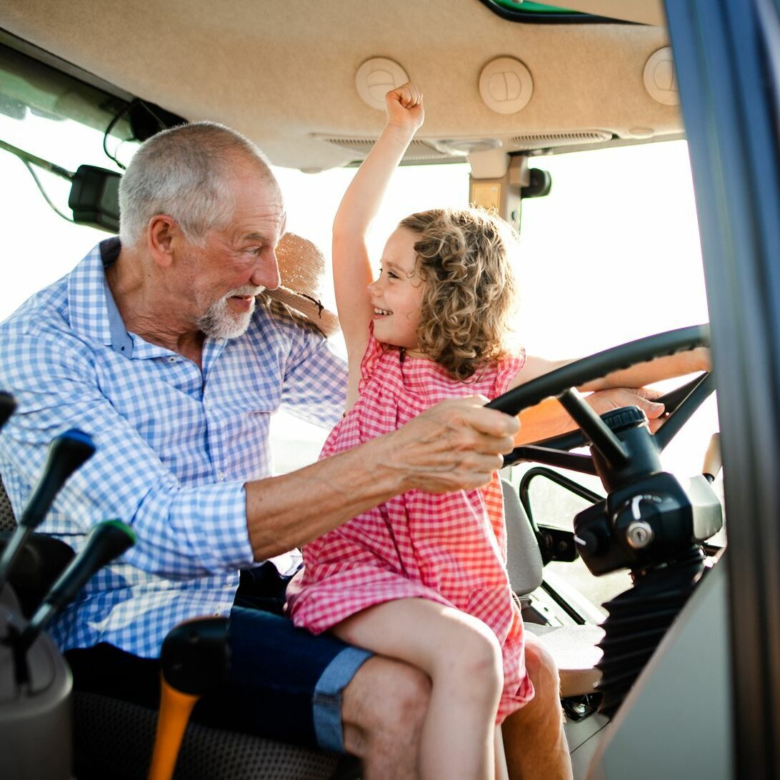 Ein alter Landwirt sitzt mit der Enkeltochter im Traktor
