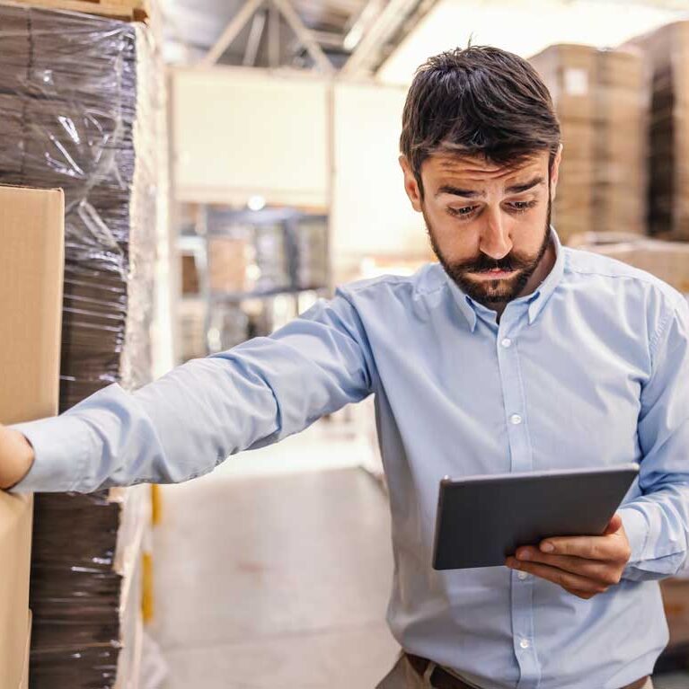 lagermitarbeiter schaut besorgt in einem Lager auf sein Tablet.